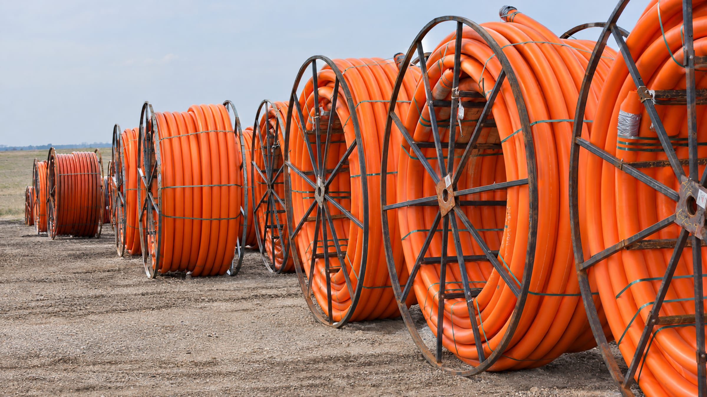 Reels of orange HDPE conduit staged for installation in an open field
