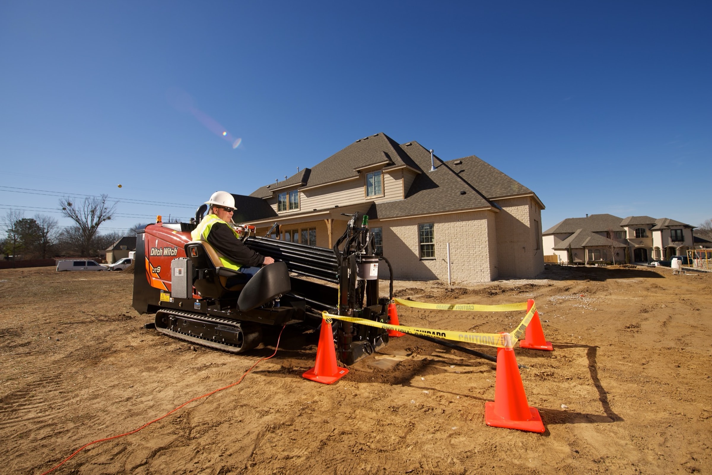 Operator running a Ditch Witch JT9 directional drill on a residential job site, with caution tape and cones in the foreground
