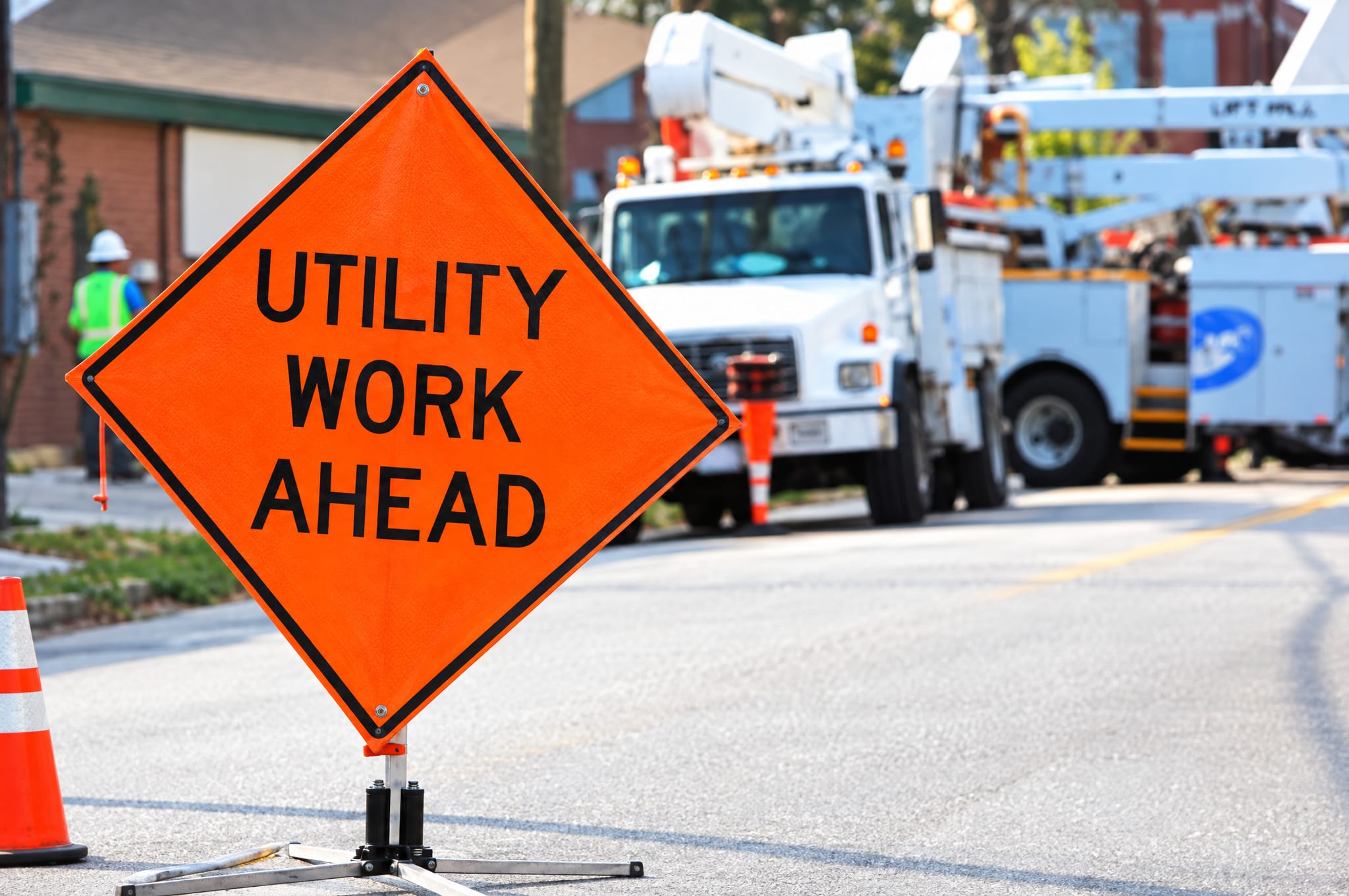 Utility work ahead sign and bucket trucks at a roadside work zone